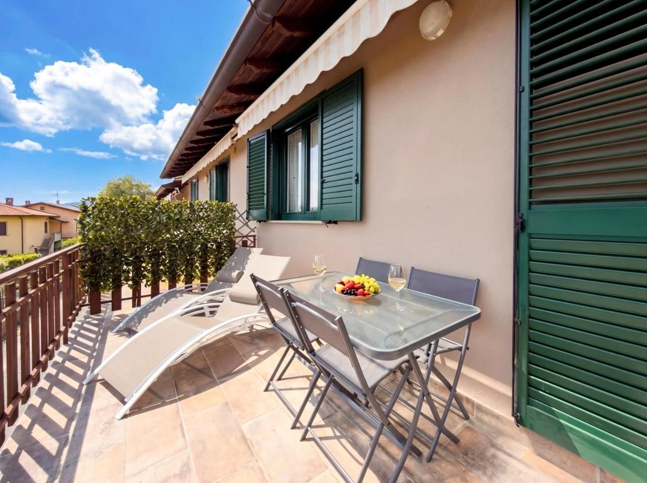 Seconda terrazza dell'appartamento con lettino prendisole, tavolo da pranzo all'aperto e persiane verdi