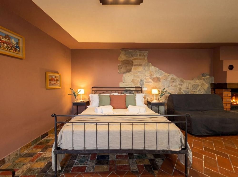 Schlafzimmer im Erdgeschoss mit schmiedeeisernem Bett, Natursteinwand und Kamin
