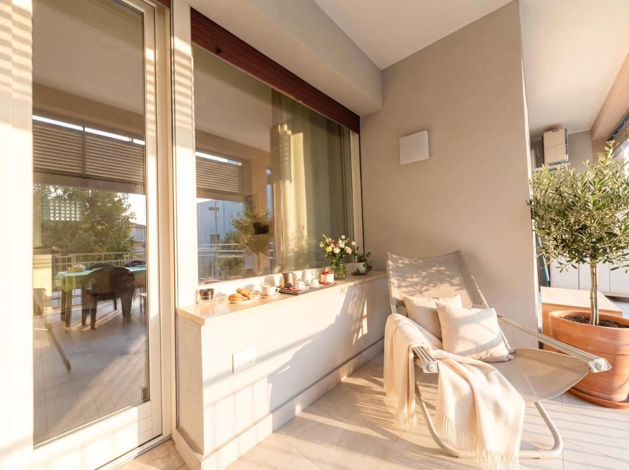 Ecke der Terrasse mit Sessel, Pflanzen und einem Olivenbaum im Topf
