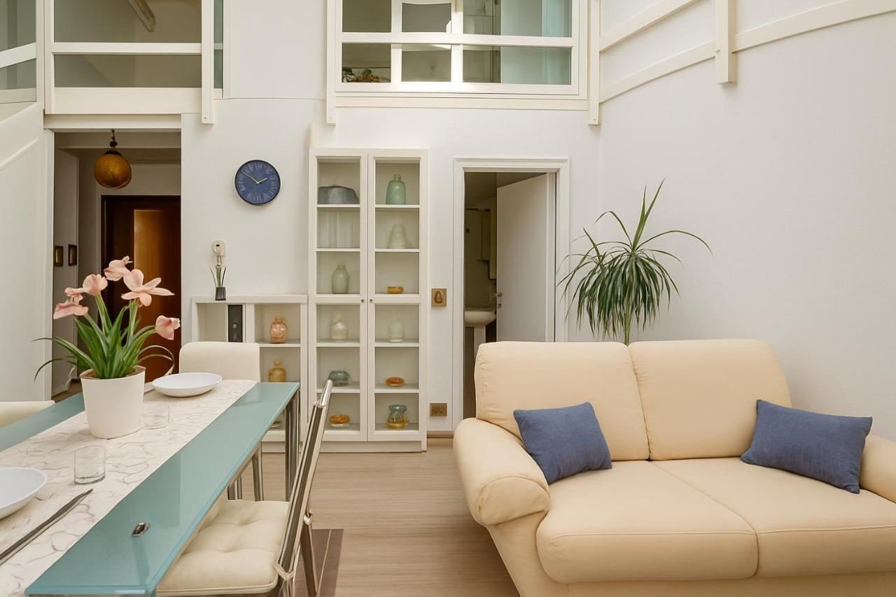 Wohnbereich mit hellem Sofa, Esstisch aus Glas und Vitrine