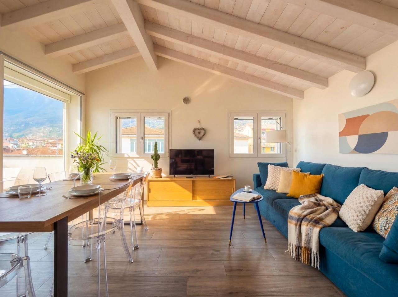 Open-plan living room with exposed beams, a blue sofa and a dining area, in the penthouse in Sale Marasino